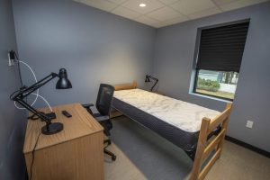 A modern bedroom setup in a triumph modular building featuring a simple desk, chair, and an unmade bed, showcasing the functionality of modular construction for both permanent and temporary modular buildings.