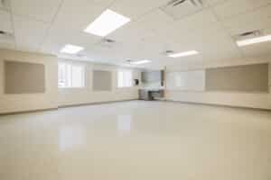 An empty classroom interior with a sink and cabinets in the far right corner.